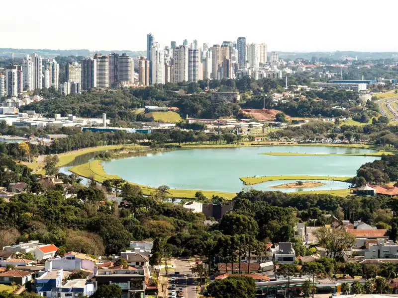 Vista panorâmica da cidade com lago e prédios modernos ao fundo, destacando a harmonia entre natureza e urbanização.