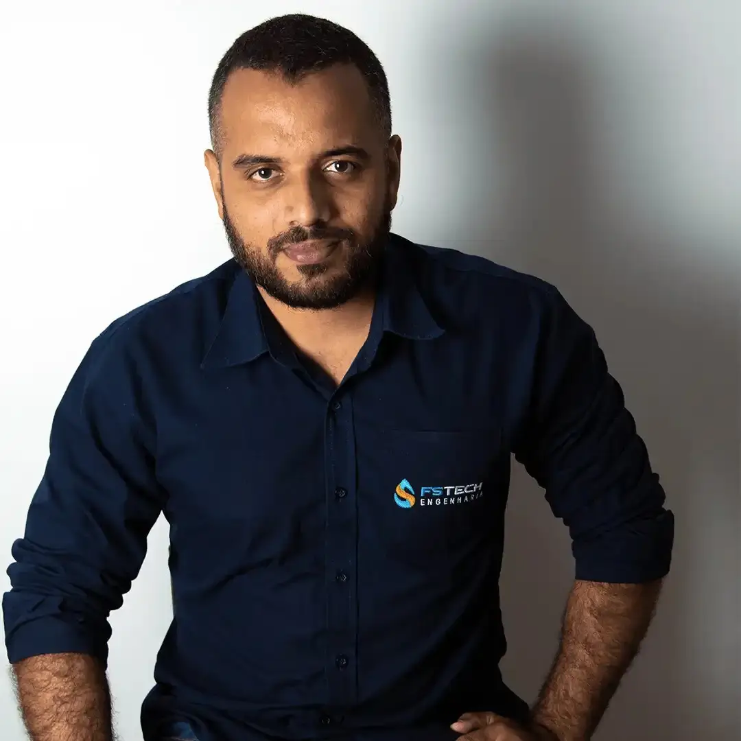 Homem de camisa escura com logo da FS Tech Engenharia, sorrindo em um fundo neutro. Ideal para ilustrar temas relacionados à engenharia e tecnologia.